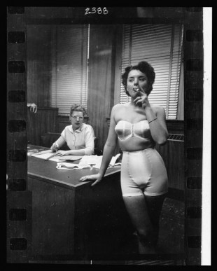21.-Lingerie-model-wearing-a-girdle-and-strapless-bra-smoking-in-an-office-in-the-background-a-woman-sits-at-a-desk