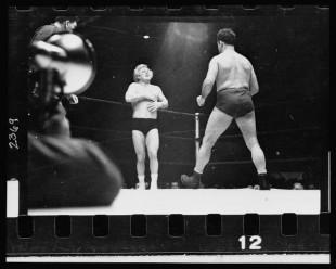 29.-A-wrestler-strides-toward-Gorgeous-George-who-stands-near-a-corner-of-the-ring-with-his-hands-on-his-chest-where-he-had-received-a-blow-in-the-previous-maneuver-in-the-wrestling-match